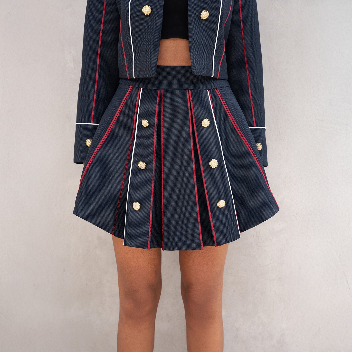 Detail of the pleated skirt from the Axis set, highlighting vertical red and white lines with golden button embellishments.