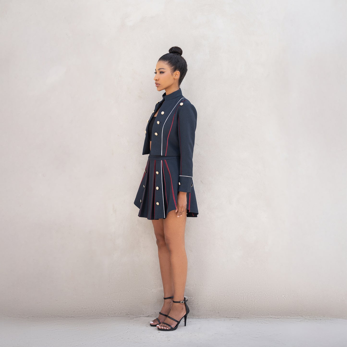 Side angle of the Axis set, showing the cropped jacket and pleated skirt with golden button detailing.