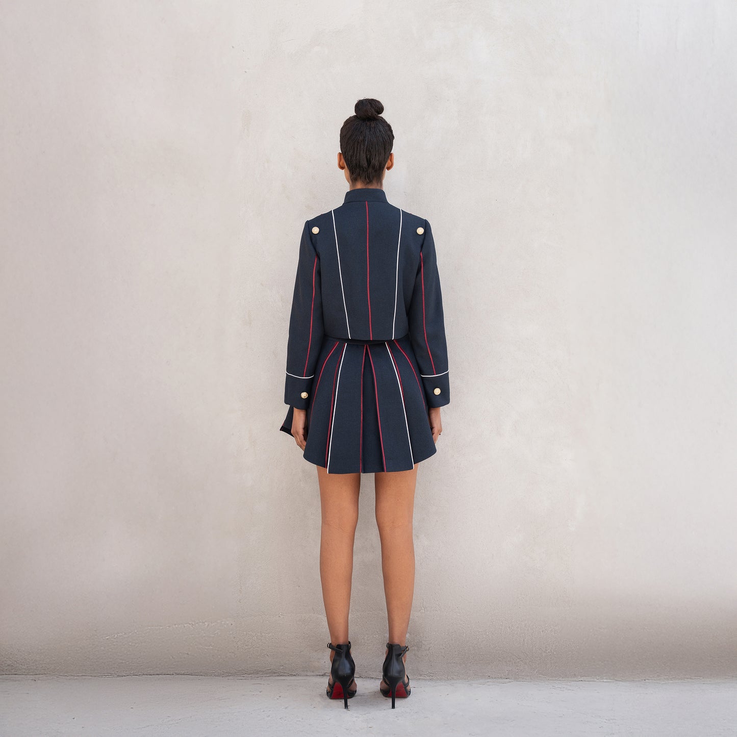 Rear view of the Axis set, showing vertical red-and-white laser-cut lines on the jacket and pleated skirt.