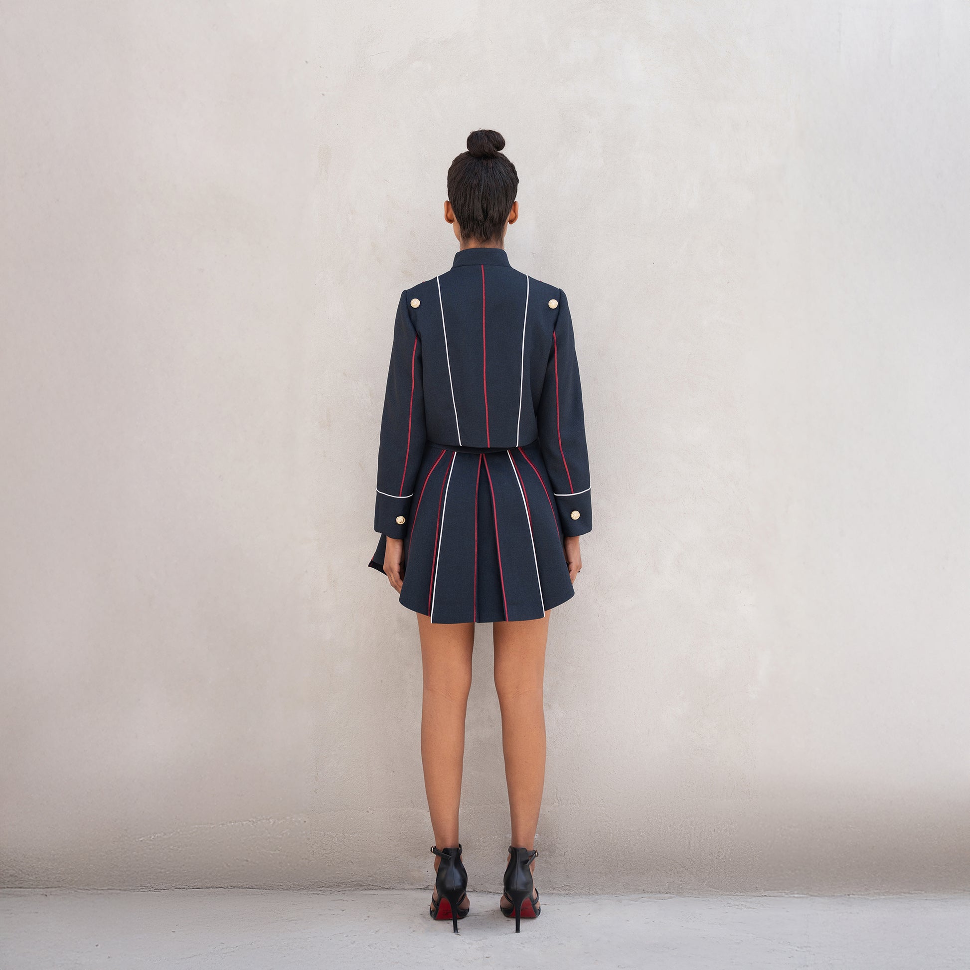 Rear view of the Axis set, showing vertical red-and-white laser-cut lines on the jacket and pleated skirt.
