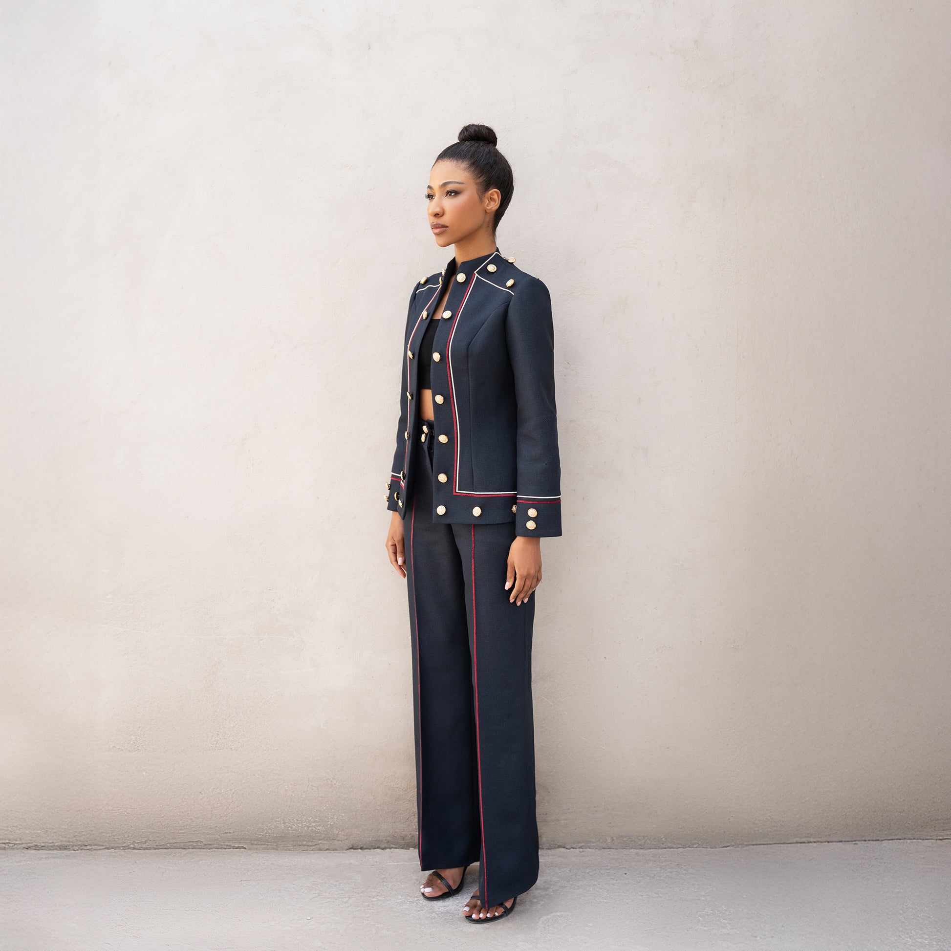 Angled view of the Frame suit showing the structured jacket with red and white line detailing and golden button accents.