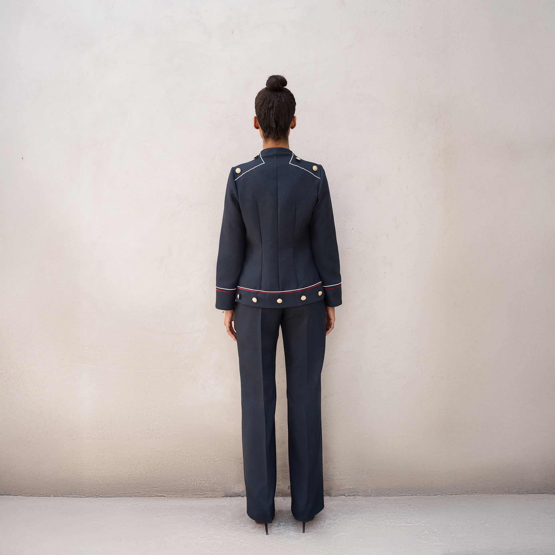Rear view of the Frame suit, showing the fitted jacket with golden button details and subtle red and white line accents.