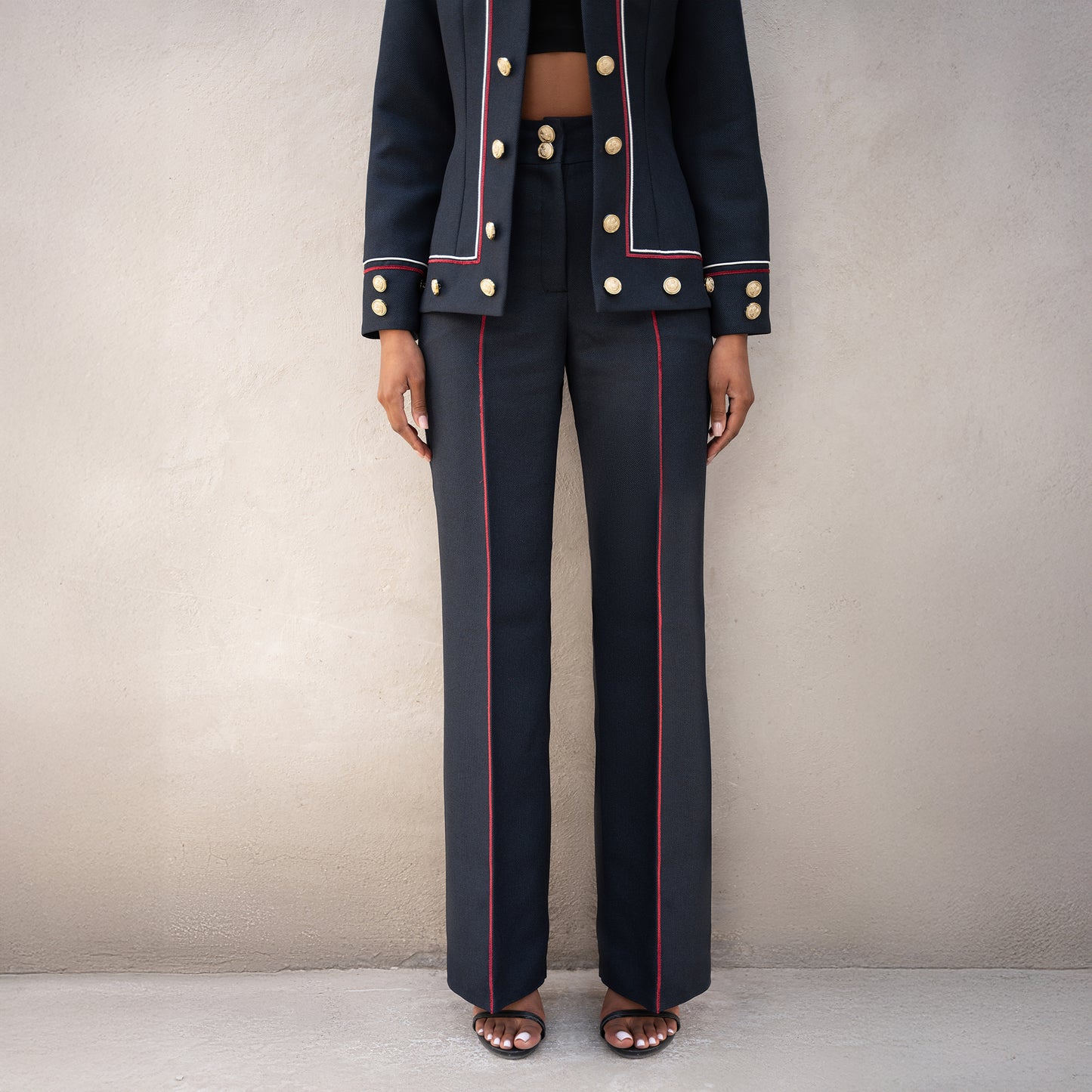 Detailed view of the Frame trousers and jacket hem, showing vertical red lines and golden button embellishments.