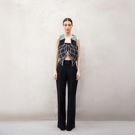 A woman wearing a sleeveless velvet vest with golden laser-cut geometric patterns inspired by the Panther Facade, featuring green velvet shoulder panels and paired with black wide-leg trousers.