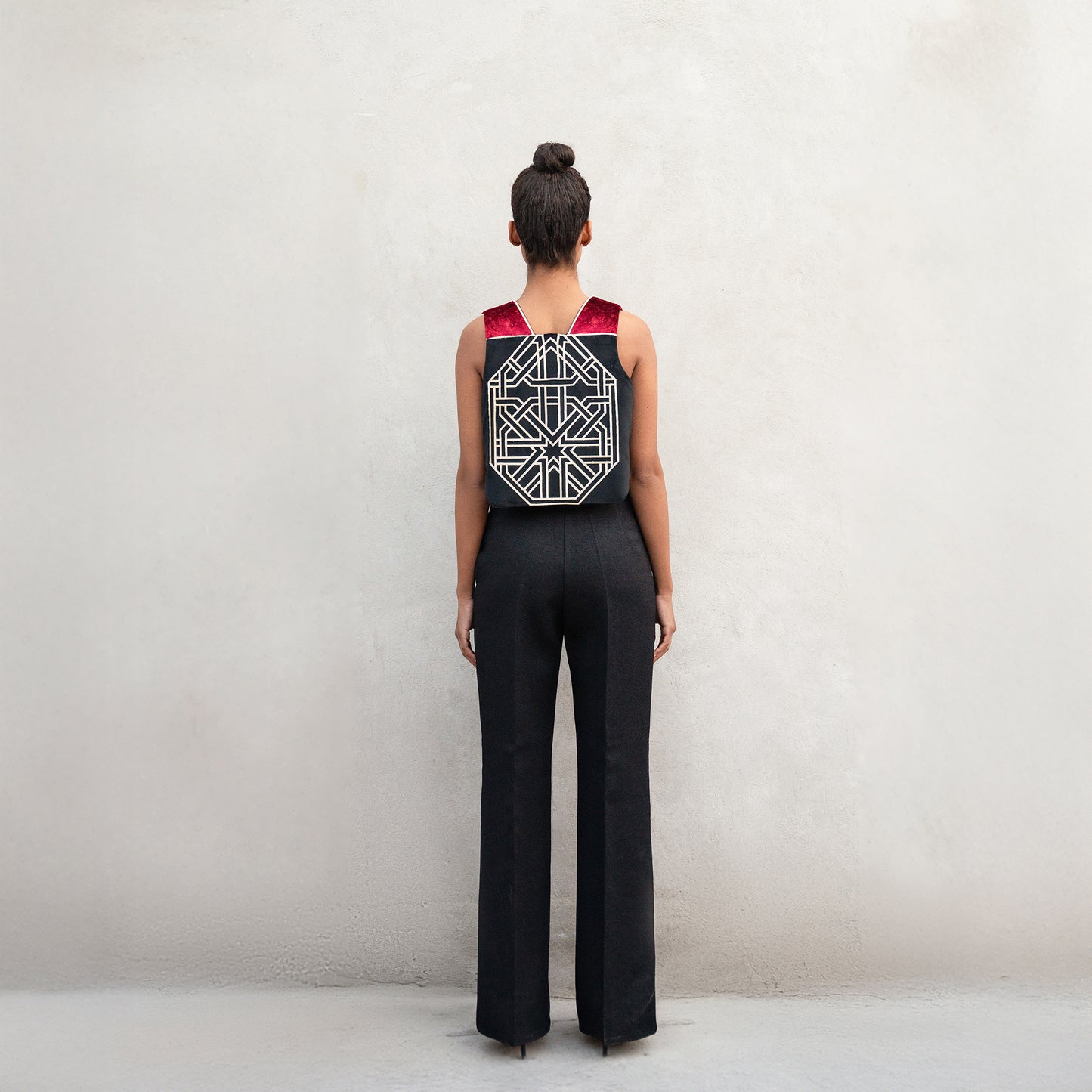 The back of the outfit, featuring a large golden laser-cut geometric design centered on the vest, paired with black high-waisted wide-leg trousers.