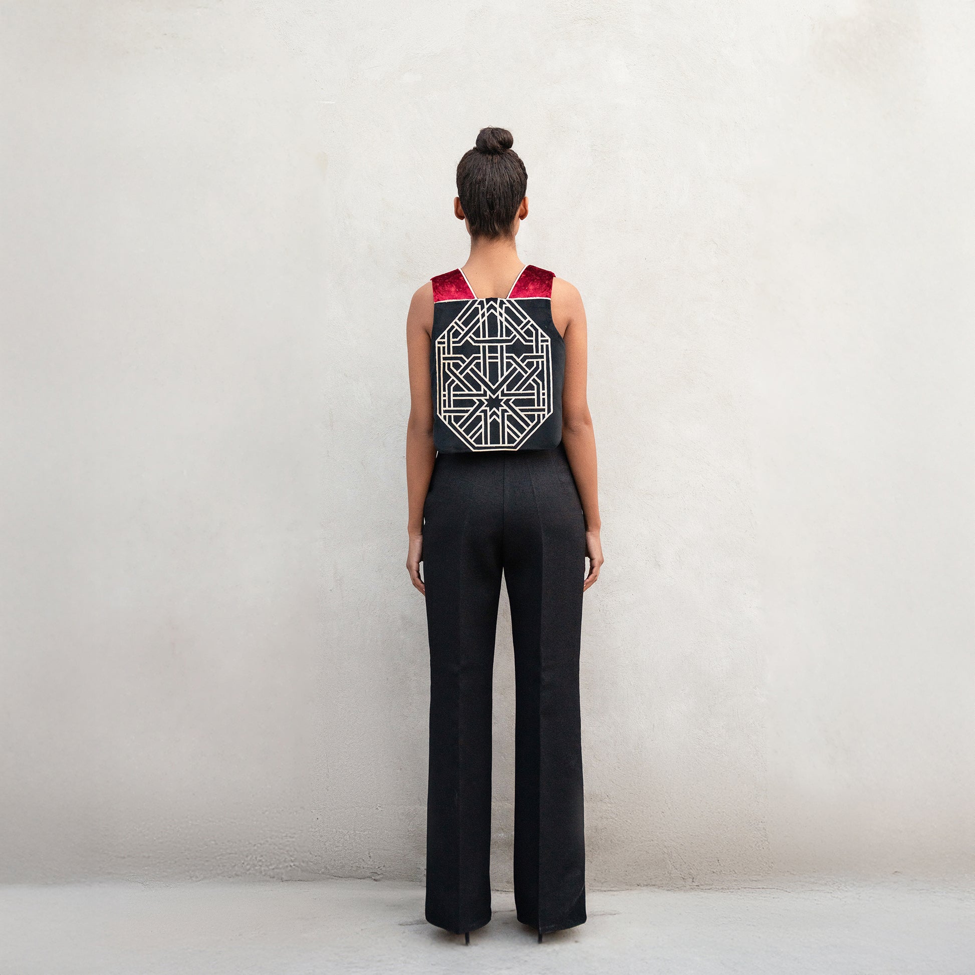 The back of the outfit, featuring a large golden laser-cut geometric design centered on the vest, paired with black high-waisted wide-leg trousers.
